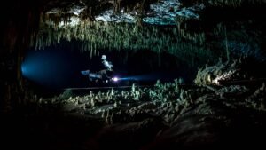 Cave diver moving through a cave passage illuminated by dive lights in Mexico.